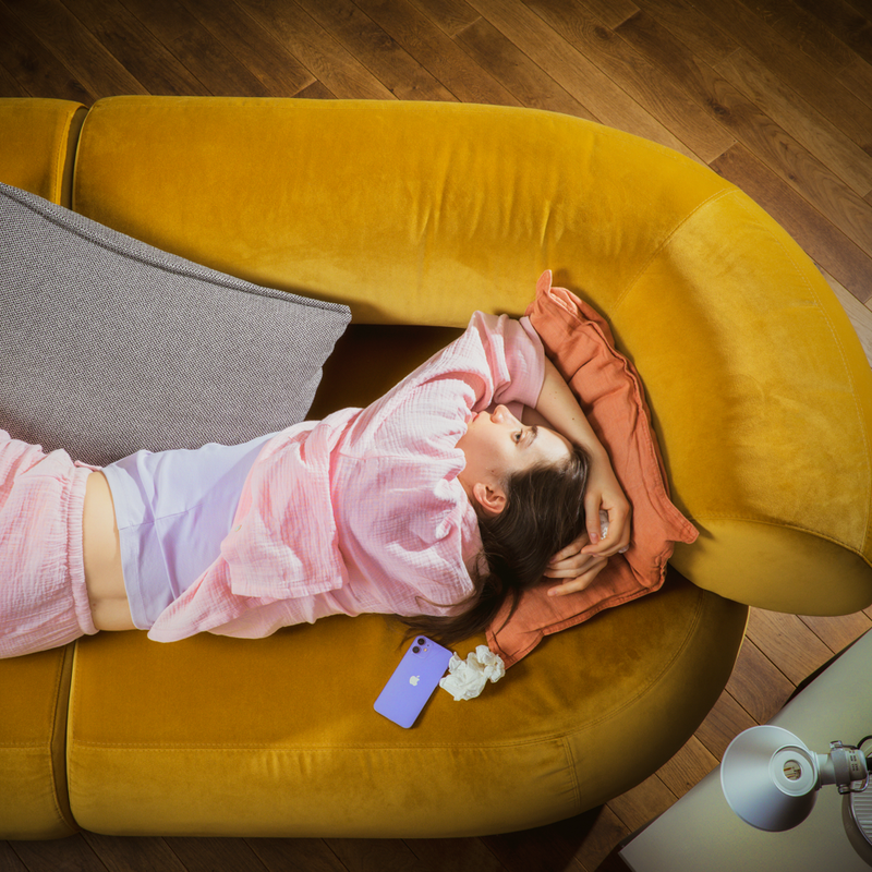 A woman lies on a couch holding her head.