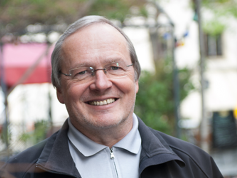 Homme souriant portant des lunettes, une veste sombre et une chemise de couleur claire