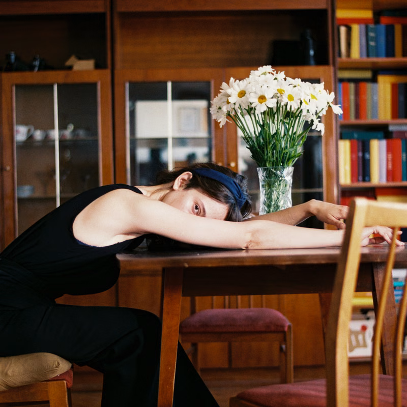 Woman resting her head on a wooden table in a cozy room with books and flowers