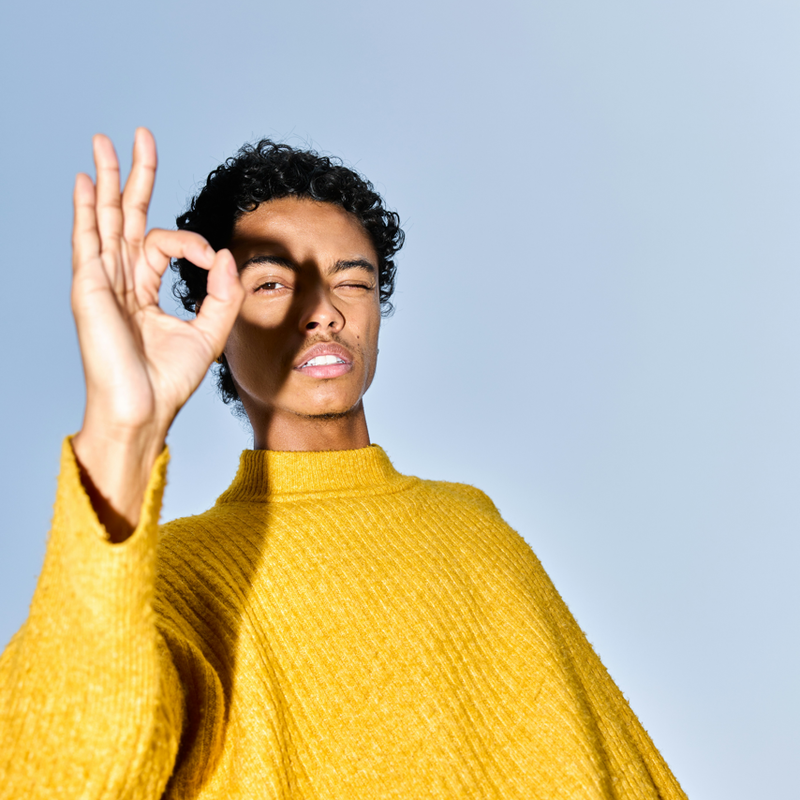 Person in gelbem Pullover, die mit der Hand ein Friedenszeichen macht