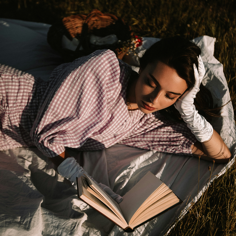 Person liegt auf einer Decke im Freien und liest ein Buch